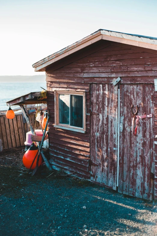 a red shed sitting next to a body of water, pexels contest winner, fishing village, inside a shed, profile image, sunfaded