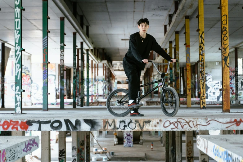 a man riding a bike on top of a wooden platform, a portrait, inspired by Seb McKinnon, in a warehouse, press shot, louise zhang, an abandoned