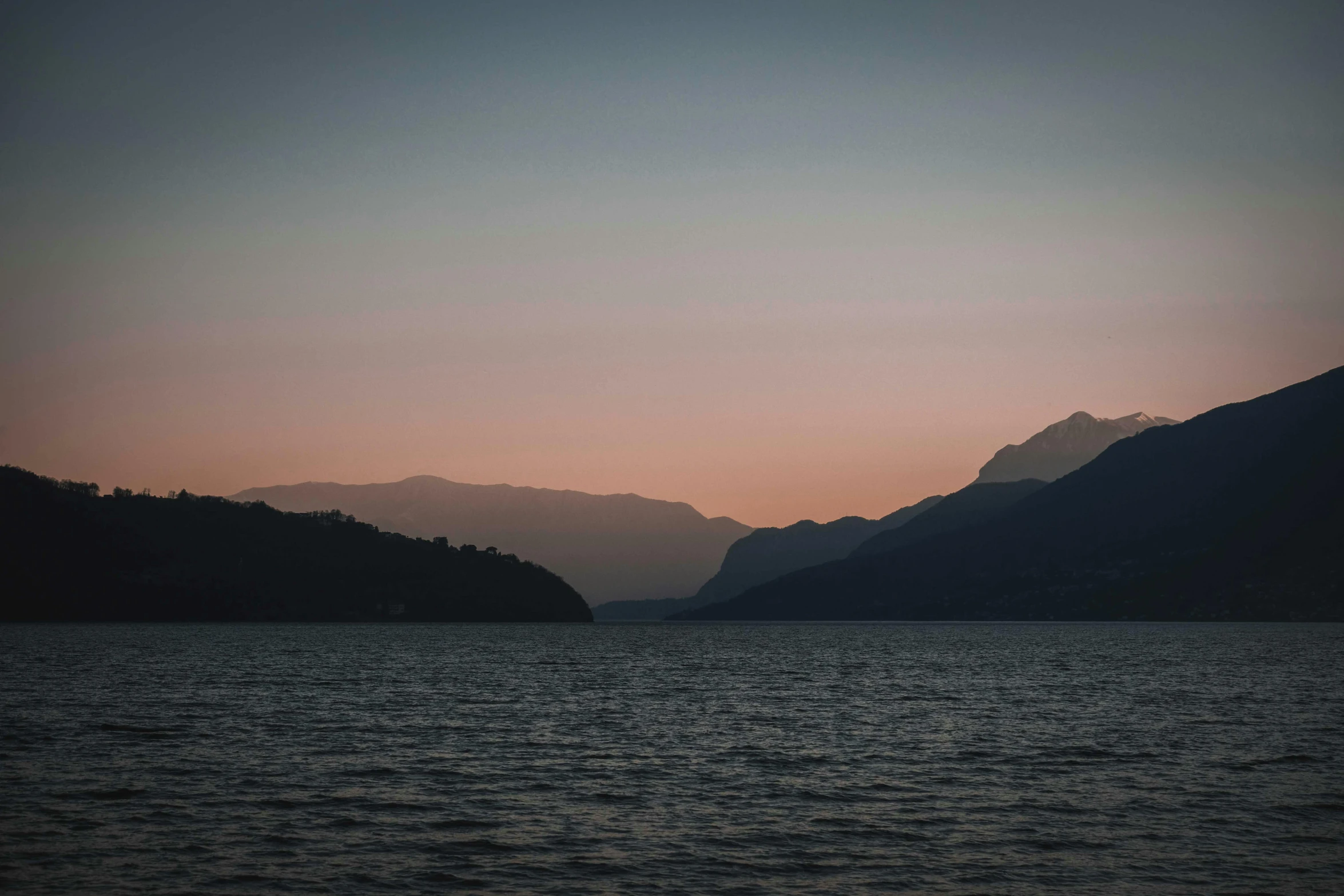 a body of water with mountains in the background, pexels contest winner, romanticism, late summer evening, faded colours, multiple stories, it's getting dark