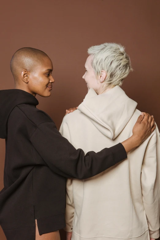 a couple of women standing next to each other, trending on unsplash, antipodeans, brown buzzcut, beige hoodie, non binary model, catalog photo