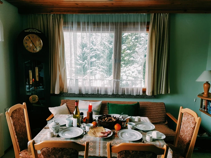 a table that has a bunch of plates on it, a still life, inspired by Elsa Bleda, pexels contest winner, wide shot of a cabin interior, carpathian mountains, holiday season, window