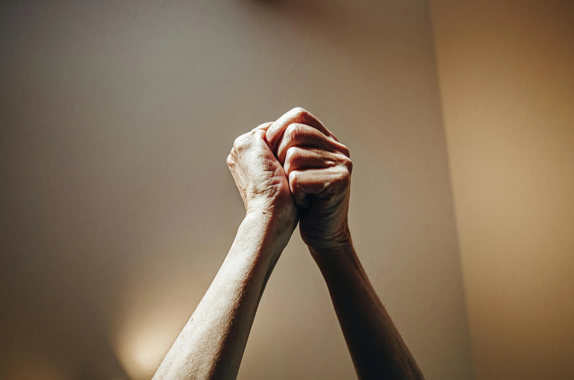 a close up of two hands holding each other, unsplash, raised fist, standing in a dimly lit room, background image, praying posture