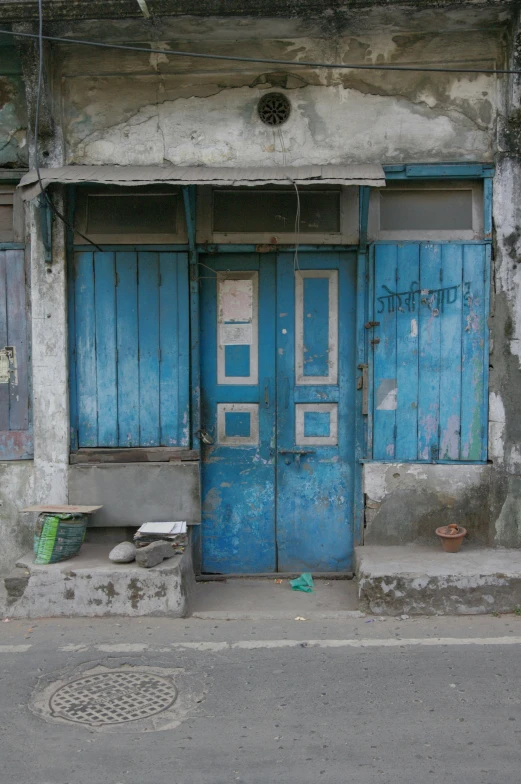 a blue door sitting on the side of a building, an album cover, flickr, bengal school of art, shanty town, old shops, but not pretty, color image