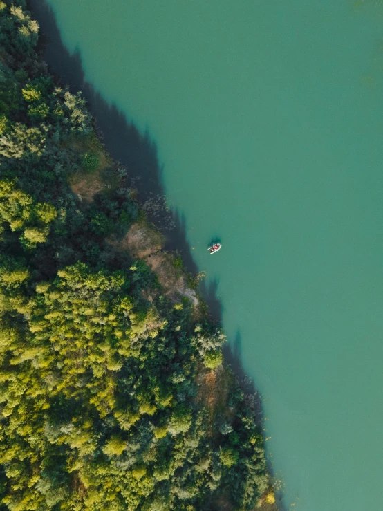 a large body of water surrounded by trees, pexels contest winner, one small boat, video still, looking down, high res 8k