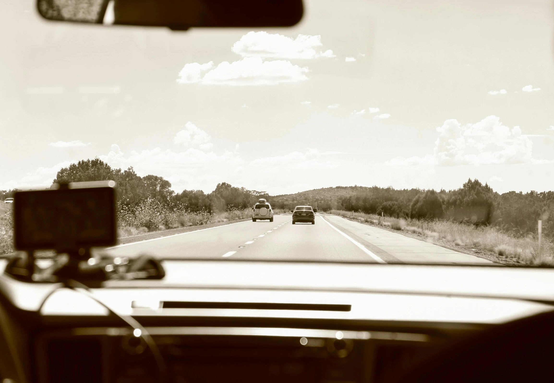 a black and white photo of a car driving down the road, an album cover, inspired by Louis Faurer, unsplash, realism, in the australian outback, sepia sunshine, car chase scene, interior shot