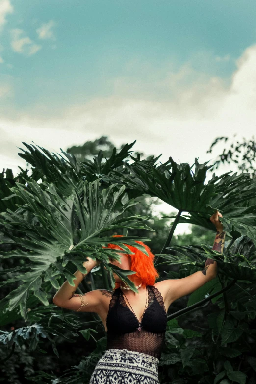 a woman standing in the middle of a lush green forest, inspired by Elsa Bleda, sumatraism, big leaf bra, orange hair, reaching for the sky, monstera deliciosa