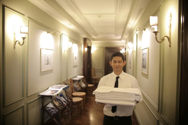 a man standing in a hallway holding a stack of folded towels, a portrait, by Gen Paul, happening, marble room, kuang hong, staff, maid