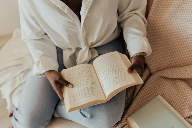 a woman sitting on a bed reading a book, by Carey Morris, pexels contest winner, happening, white shirt and blue jeans, maria borges, sustainable materials, muted and pastel shades