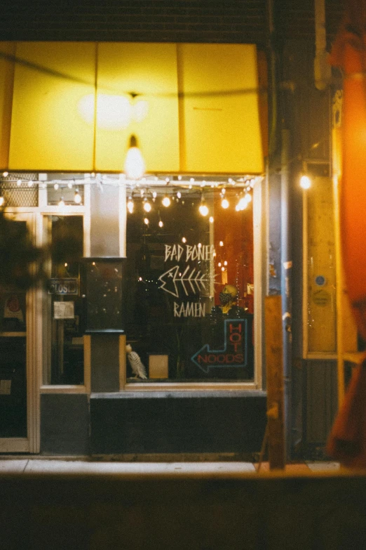 a person walking in front of a store at night, restaurant, warm yellow lights, window open, local bar