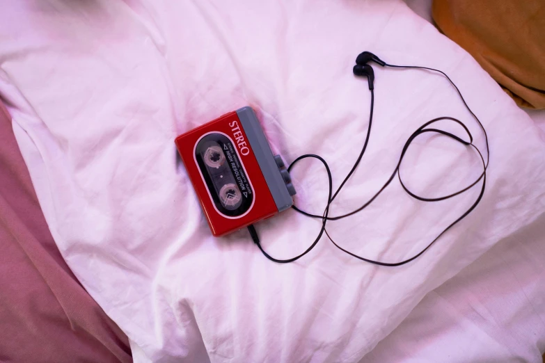a red cassette player sitting on top of a bed, pink headphones, bed, pink, cassette tape