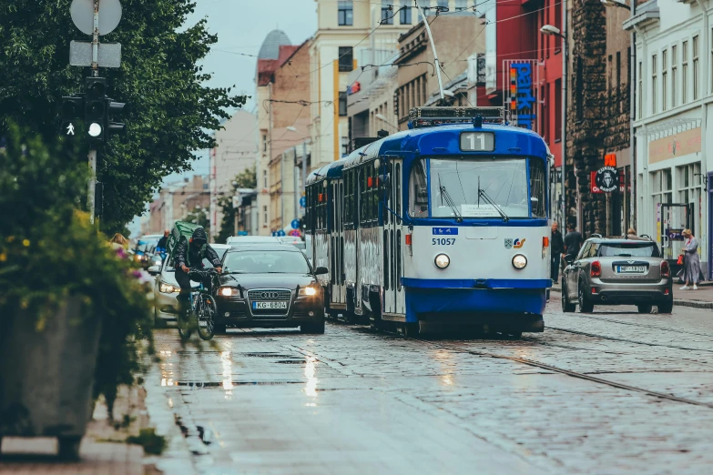 a blue and white bus driving down a street, by Adam Marczyński, pexels contest winner, after rain, kama russian electrocar, trams ) ) ), square