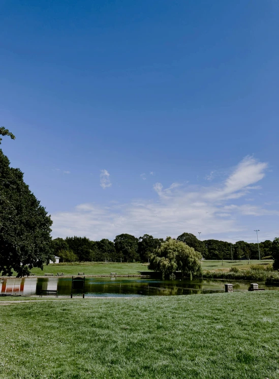 a man flying a kite on top of a lush green field, in a park and next to a lake, brockholes, clear blue skies, today\'s featured photograph 4k