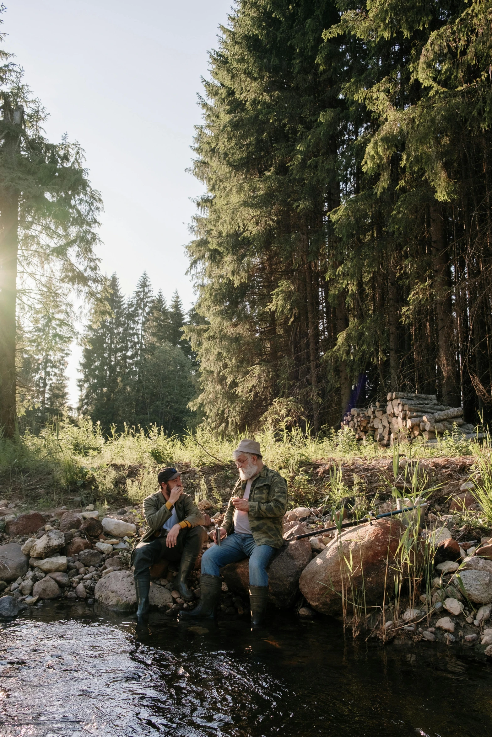 a group of people sitting on rocks next to a river, hunting, pine forests, sundown, viktor orban in a forest