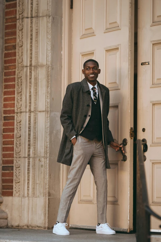 a man is standing in front of a door, inspired by Harrington Mann, trending on unsplash, adut akech, academic clothing, gray men, well - dressed