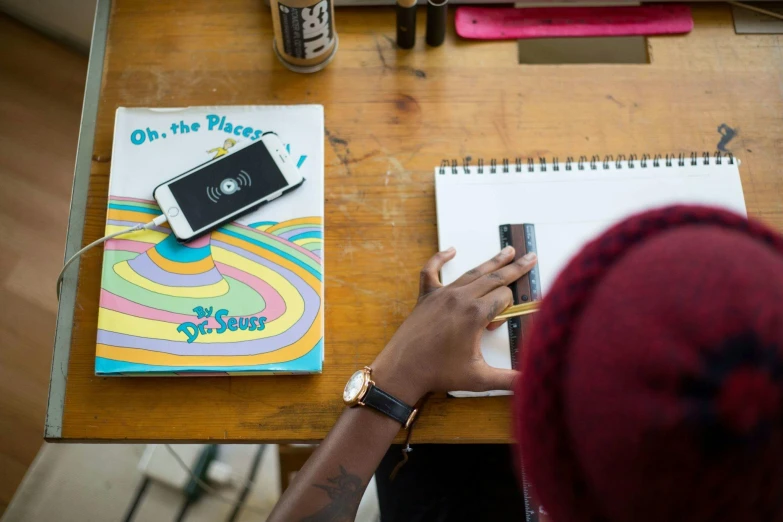 a person sitting at a table with a cell phone, process art, holding notebook, 9 9 designs, student, top - down photograph