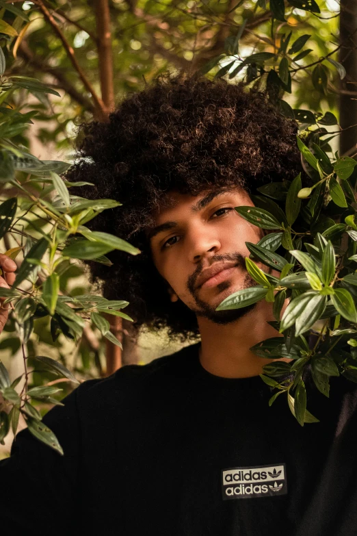 a man with curly hair standing in front of a tree, pexels contest winner, funk art, lush plant growth, handsome hip hop young black man, middle eastern, greens)