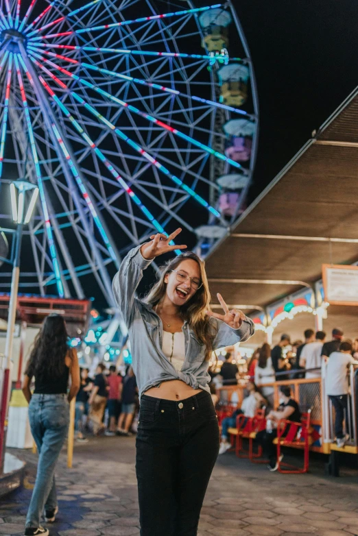 a woman standing in front of a ferris wheel at night, earing a shirt laughing, sydney sweeney, with street food stalls, unsplash photography