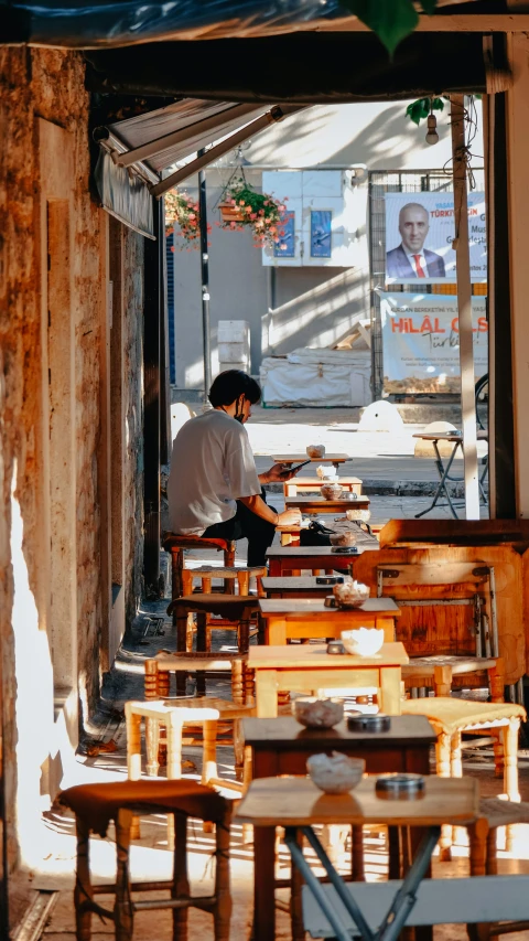 a person sitting at a table in a restaurant, by Niko Henrichon, trending on unsplash, istanbul, shop front, sunny morning, a wooden