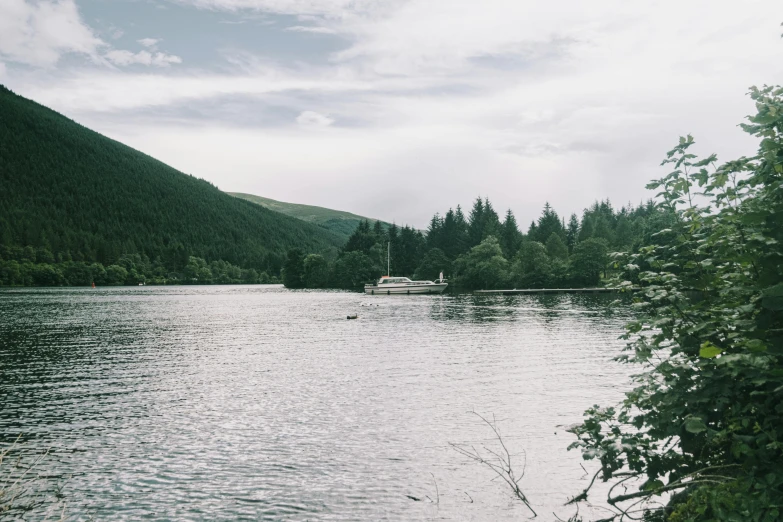 a body of water surrounded by trees and mountains, by Bedwyr Williams, ship on lake, grainy filter, low quality photo, aly fell