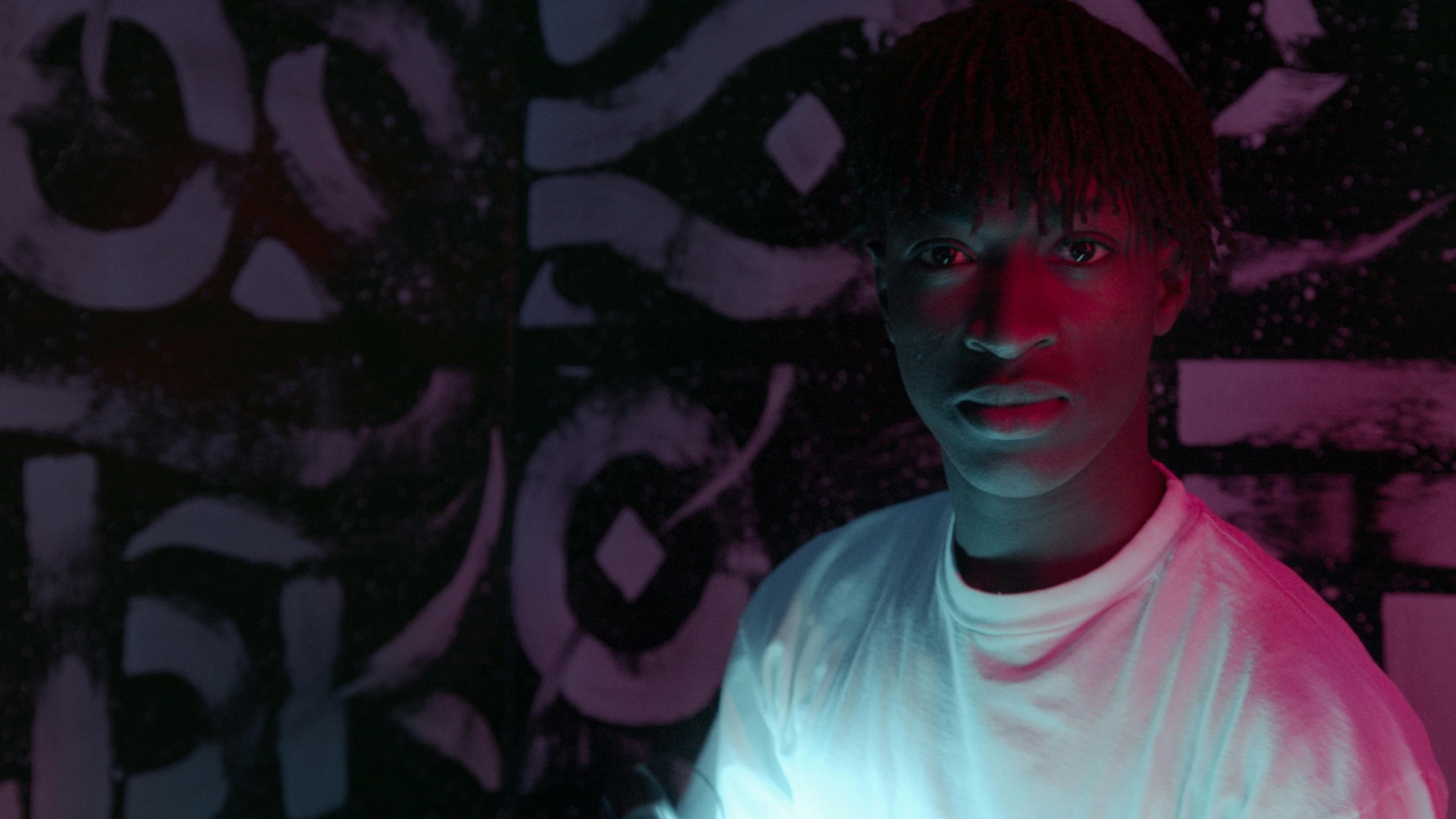 a man standing in front of a wall covered in graffiti, an album cover, inspired by Xanthus Russell Smith, pexels contest winner, afrofuturism, glowing with colored light, black teenage boy, 2 0 2 1 cinematic 4 k framegrab, lil uzi vert