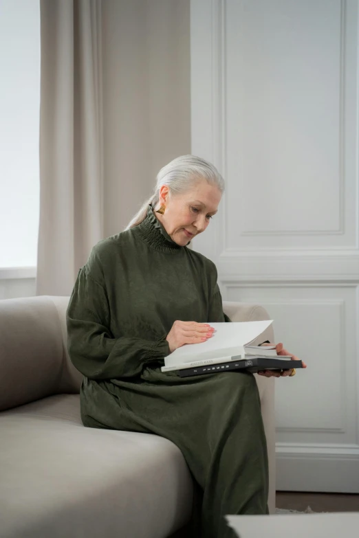 a woman sitting on a couch reading a book, a portrait, pexels contest winner, silver haired, green and brown clothes, profile image, maintenance