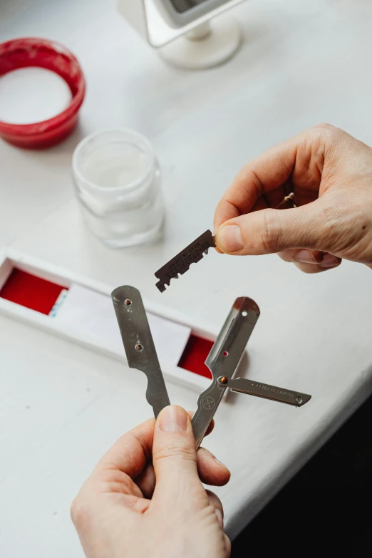 a close up of a person holding a pair of scissors, by Jacob Toorenvliet, process art, blood collection vials, metal key for the doors, on a white table, indigo and red iron oxide