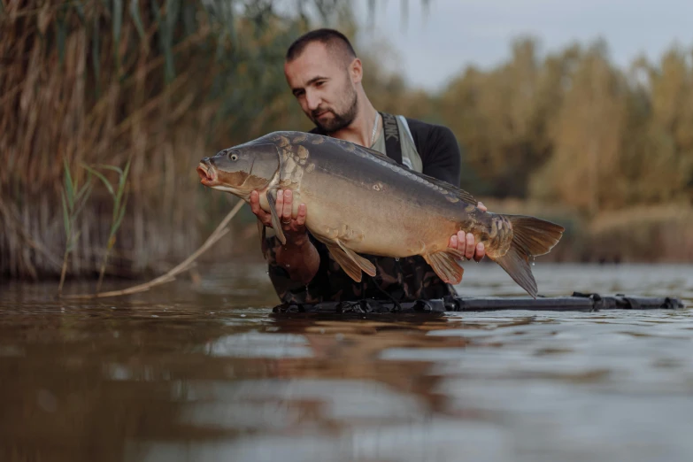 a man holding a fish in a body of water, in a pond, lpoty, with a very large mouth, bulky build