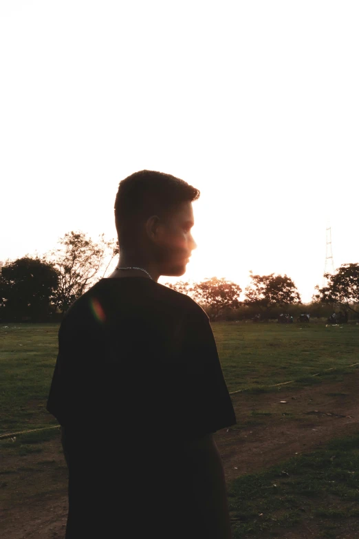 a person standing in a field with a kite in the sky, an album cover, unsplash, happening, black teenage boy, looking off into the sunset, grainy low quality, in a city park