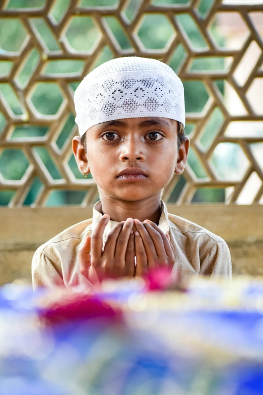 a young boy wearing a white hat and praying, pexels contest winner, hurufiyya, looking towards camera, panels, hindu, print ready