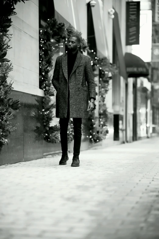 a black and white photo of a man walking down a street, inspired by Theo Constanté, wearing festive clothing, elegantly posing over you, black man, coat