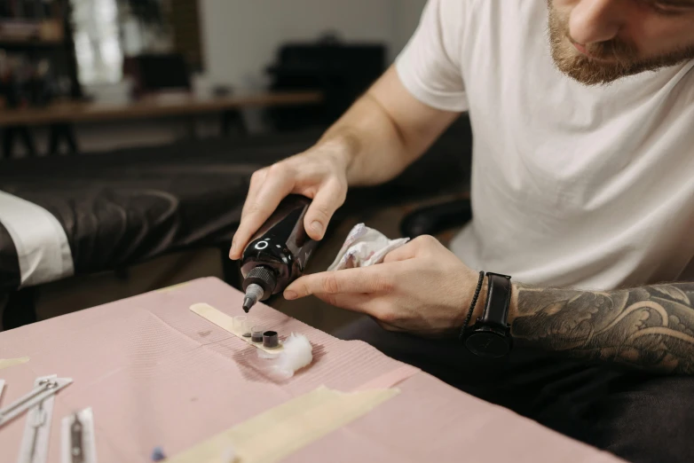 a man sitting at a table with a bottle of alcohol, trending on pexels, hyperrealism, holding a magic needle, with electric arc device, fabric embroidery, silicone skin