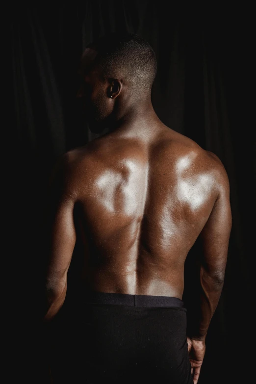 a man standing with his back to the camera, by Jessie Alexandra Dick, pexels contest winner, pitch black skin, in a gym, plain background, oiled skin