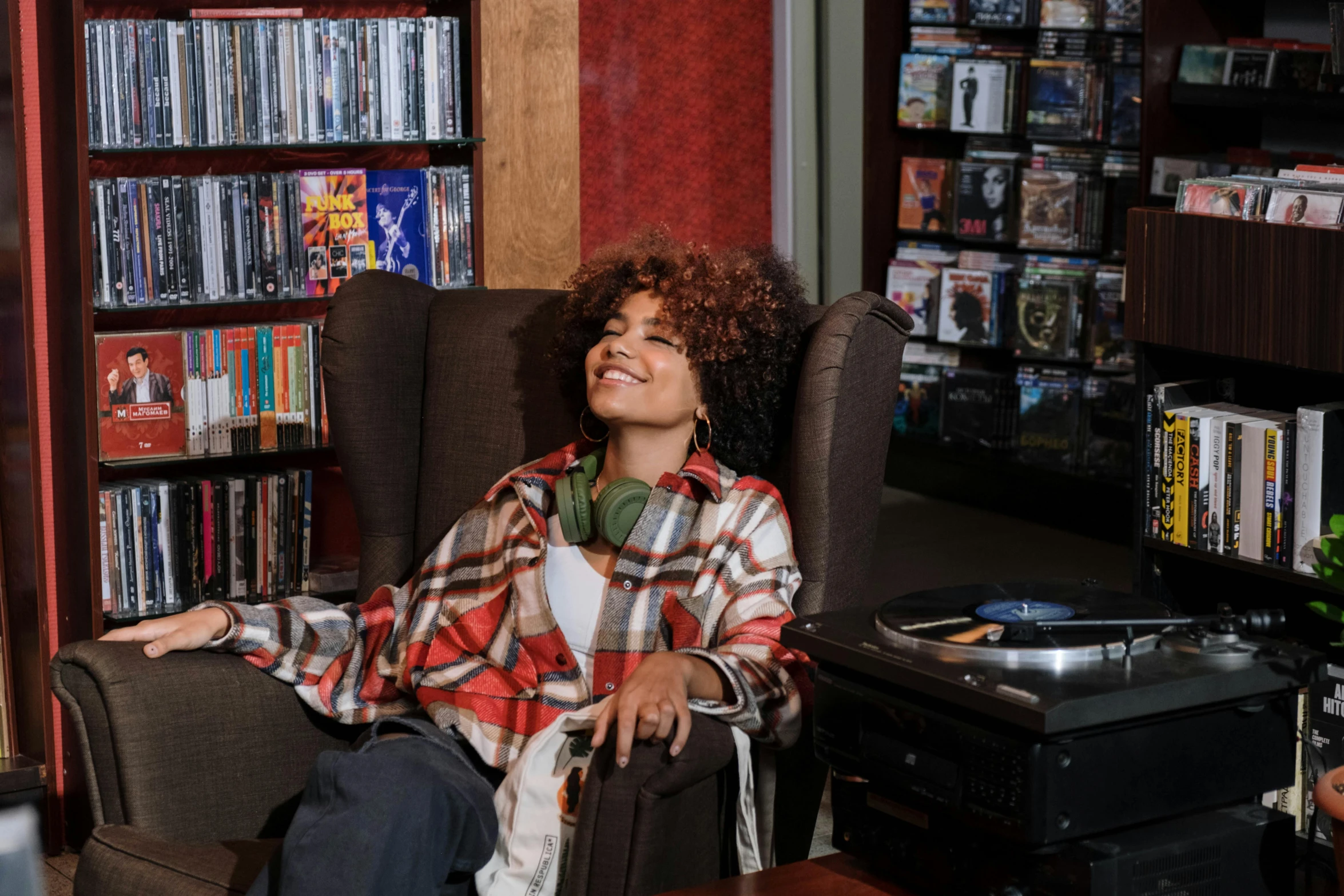 a woman sitting in a chair with headphones on, pexels, maximalism, curly haired, girl in a record store, sitting in a lounge, tessa thompson inspired