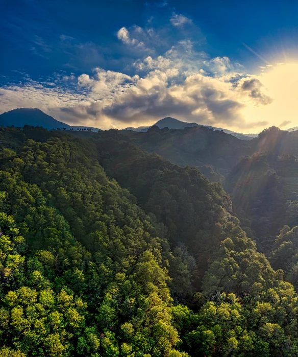 the sun shines through the clouds over the mountains, a matte painting, unsplash contest winner, sumatraism, lush trees and flowers, azores, drone photograpghy, ultrawide angle cinematic view