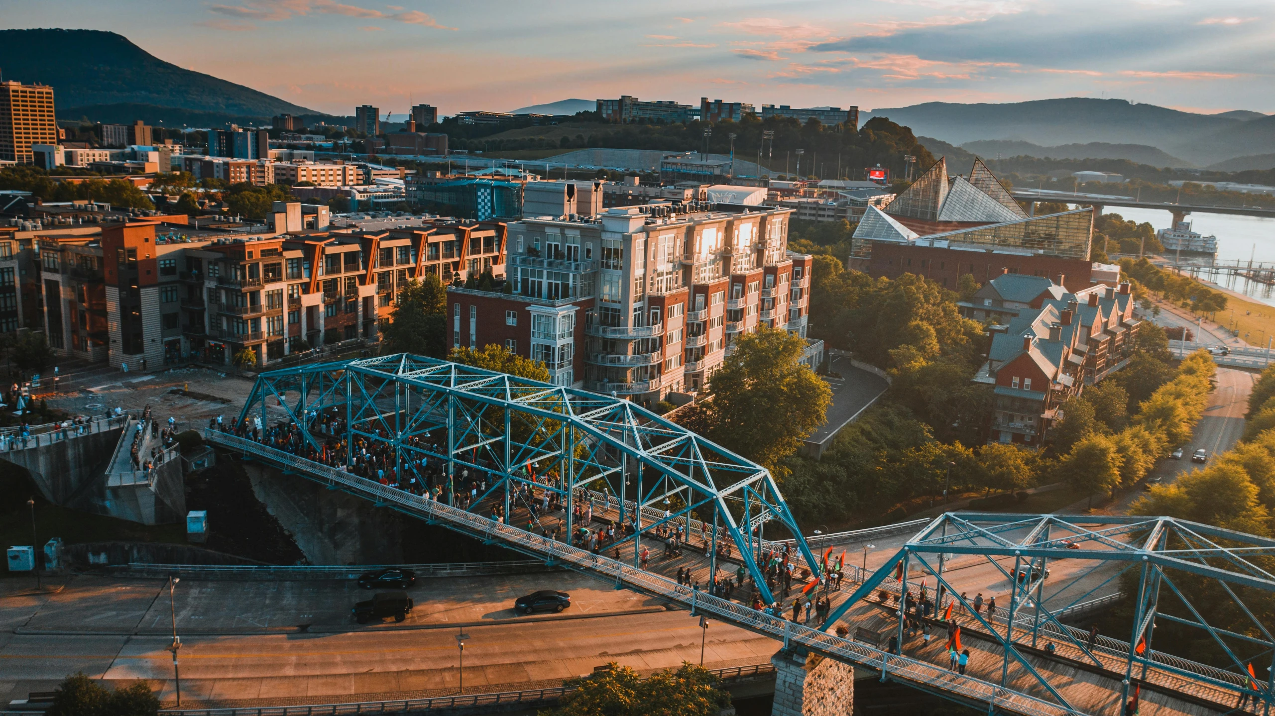 a bridge over a river with a city in the background, a photo, by Dan Frazier, pexels contest winner, happening, tn, wide aerial shot, walking down, festivals