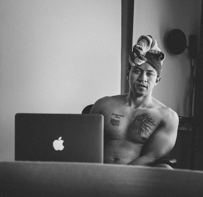 a shirtless man sitting in front of a laptop computer, a black and white photo, inspired by I Ketut Soki, unsplash, turban, posing as a jojo character, wearing a towel, people with mohawks