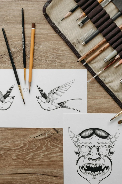 a couple of drawings sitting on top of a wooden table, an ink drawing, trending on pexels, sparrows, sailor jerry tattoo flash, pencils, symmetry illustration