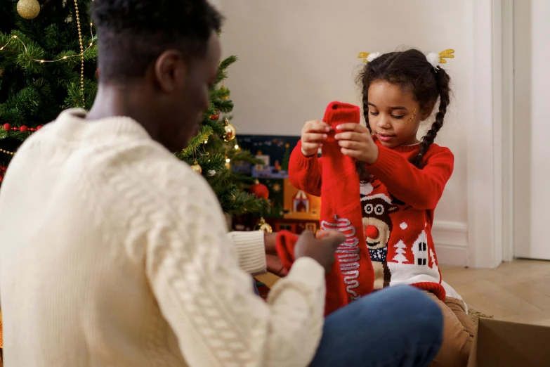 a man and a little girl sitting in front of a christmas tree, pexels contest winner, red clothes, playing games, sweater, ( ( dark skin ) )