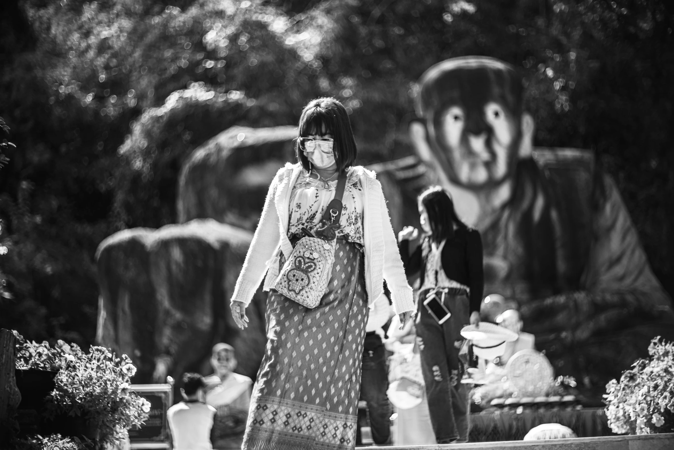 a black and white photo of a woman in a dress, a black and white photo, inspired by Garry Winogrand, unsplash, graffiti, sukhothai costume, taken in silver dollar city, people are wearing masks, walking at the garden