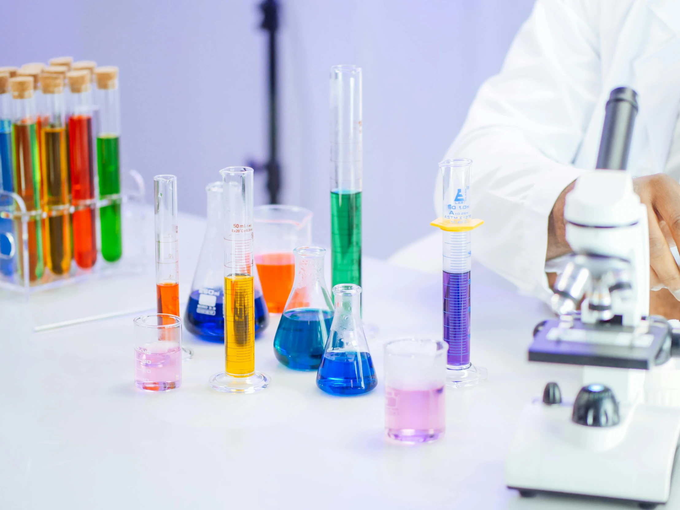 a person in a lab coat using a microscope, pexels, beakers of colored liquid, vases and bottles, schools, purple and blue and green colors