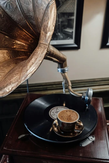 a record player sitting on top of a table next to a cup of coffee, gentleman's club lounge, bronze, two horns, medium closeup