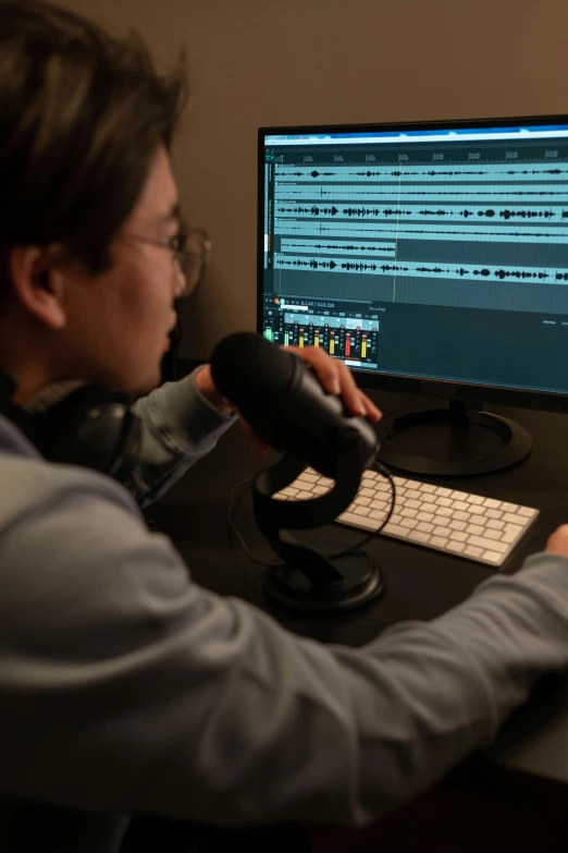 a man sitting at a desk in front of a computer, an album cover, by Dan Content, pexels, studio microphone, programming, leslie zhang, pinnacle studio