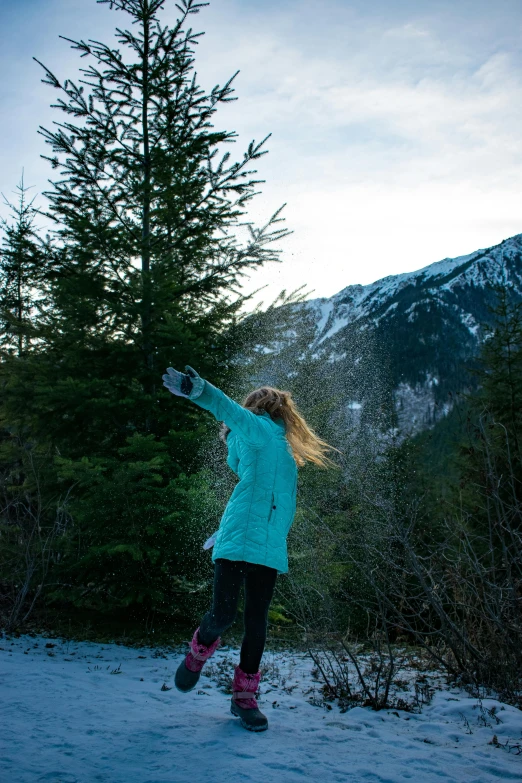 a woman standing on top of a snow covered slope, by Jessie Algie, unsplash, swaying trees, with mountains in background, fists in the air, colour photo