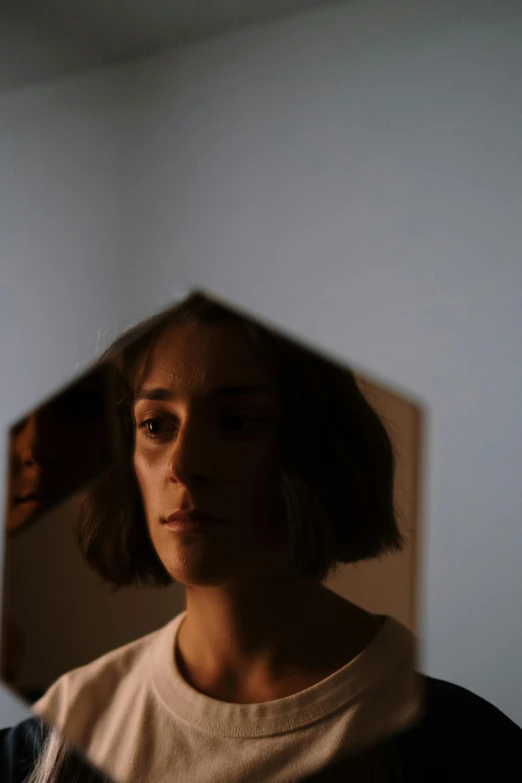 a woman standing in front of a mirror, inspired by Nan Goldin, pexels contest winner, hyperrealism, angular face, looking through a portal, cardboard, low lighting