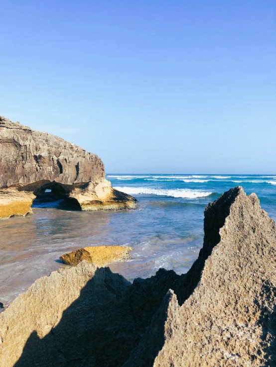 a man riding a surfboard on top of a sandy beach, rock formations, marsden, grotto, views to the ocean