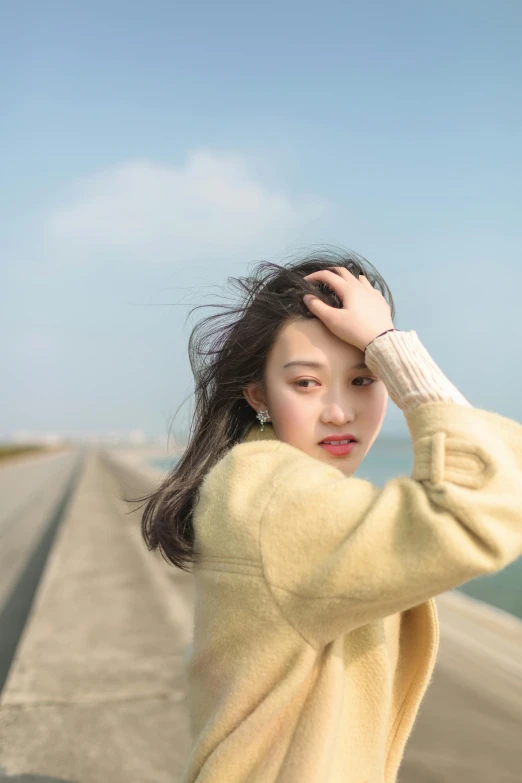 a woman standing on top of a pier next to the ocean, inspired by Tang Yifen, trending on pexels, realism, young cute wan asian face, wearing a sweater, slight yellow hue, modeling photography