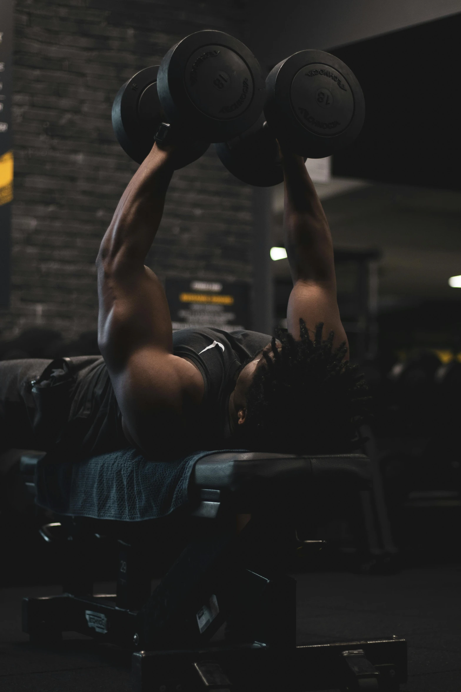 a man doing dumb curls on a bench in a gym, pexels contest winner, man is with black skin, background image, dark backround, gif