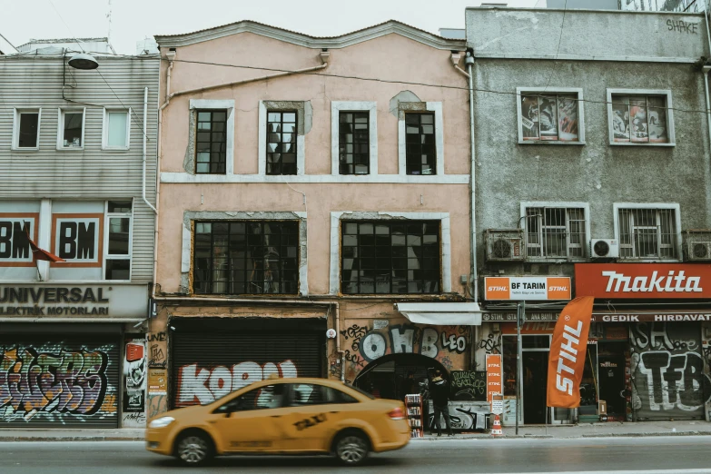 a yellow taxi driving down a street next to tall buildings, a photo, inspired by Elsa Bleda, pexels contest winner, art nouveau, turkey, old abandoned building, gray and orange colours, thumbnail