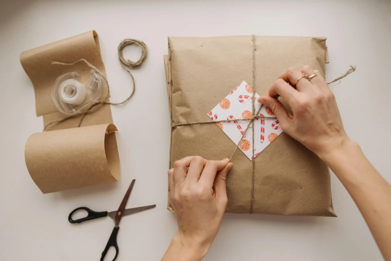 a person cutting a piece of paper with a pair of scissors, by Eden Box, pexels contest winner, arts and crafts movement, birthday wrapped presents, back facing, packaging design, on a canva