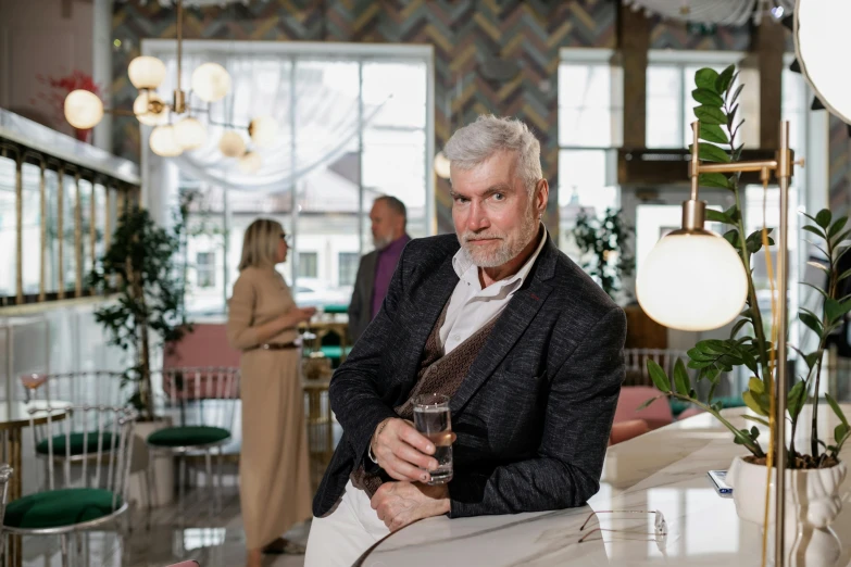 a man sitting at a table with a glass of wine, gray haired, jovana rikalo, in a bright cafe, rich evans